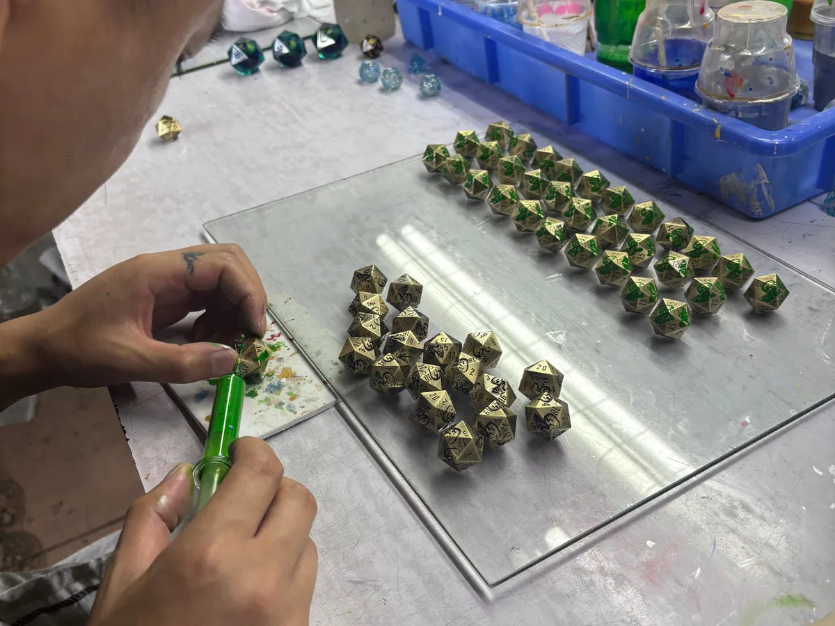 Worker hand coloring numbers on plated metal dice