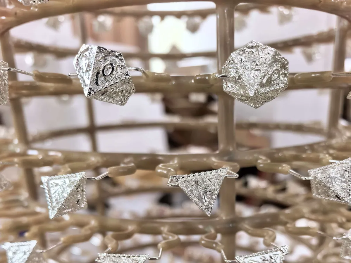 Metal d20 and d4 dice suspended on racks during electroplating
