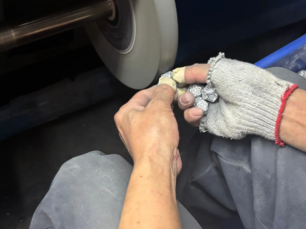 Worker polishing metal polyhedral dice at a buffing wheel