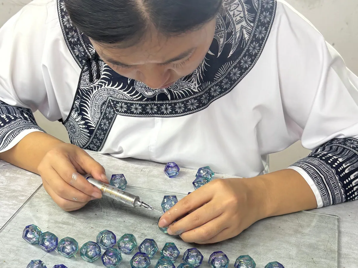 Worker coloring engraved numbers on blue and purple resin dice